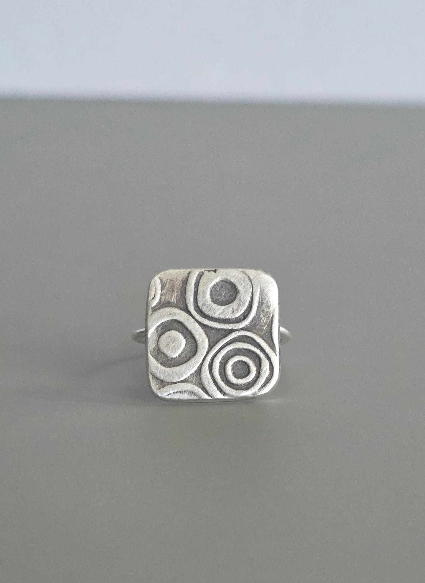 Silver ring with circular pattern on a gray background