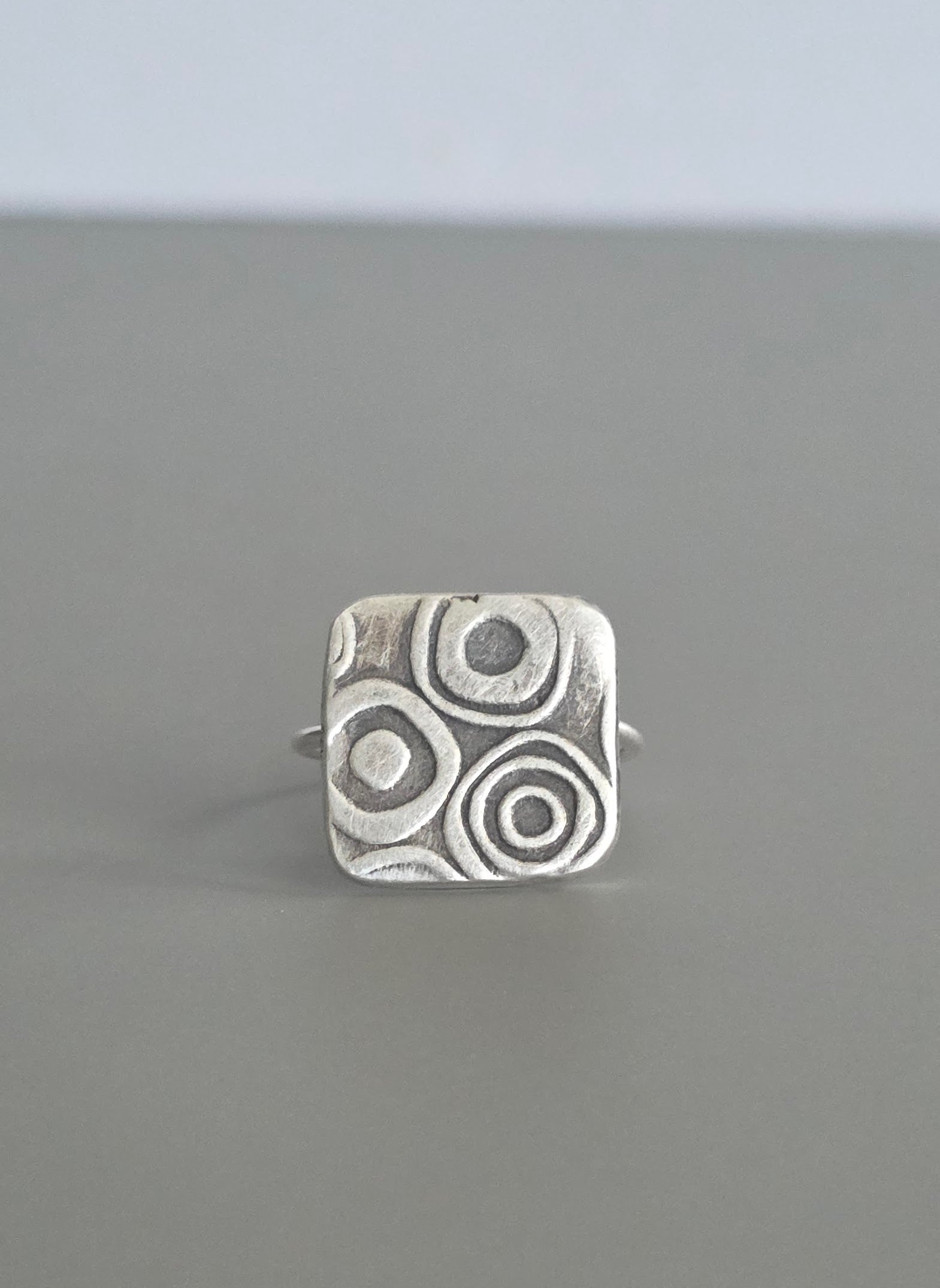 Silver ring with circular pattern on a gray background