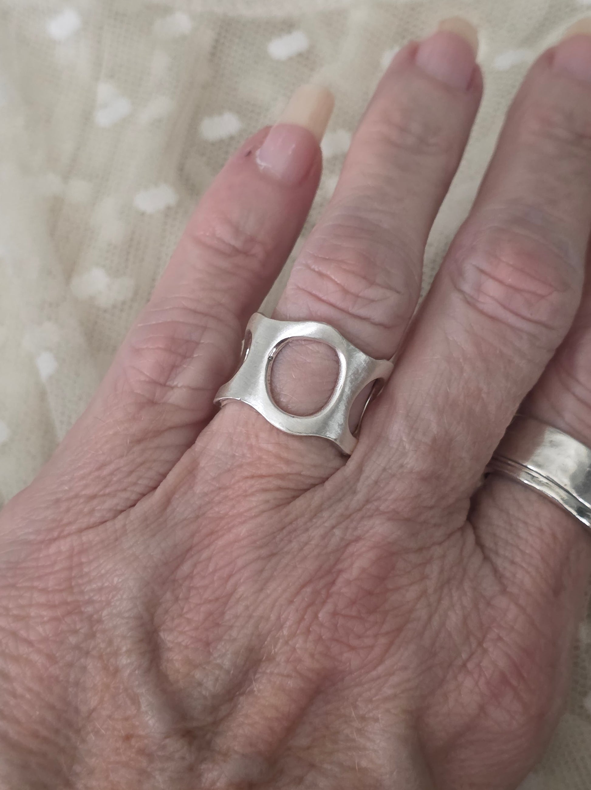 Hand wearing a silver ring on a textured fabric background