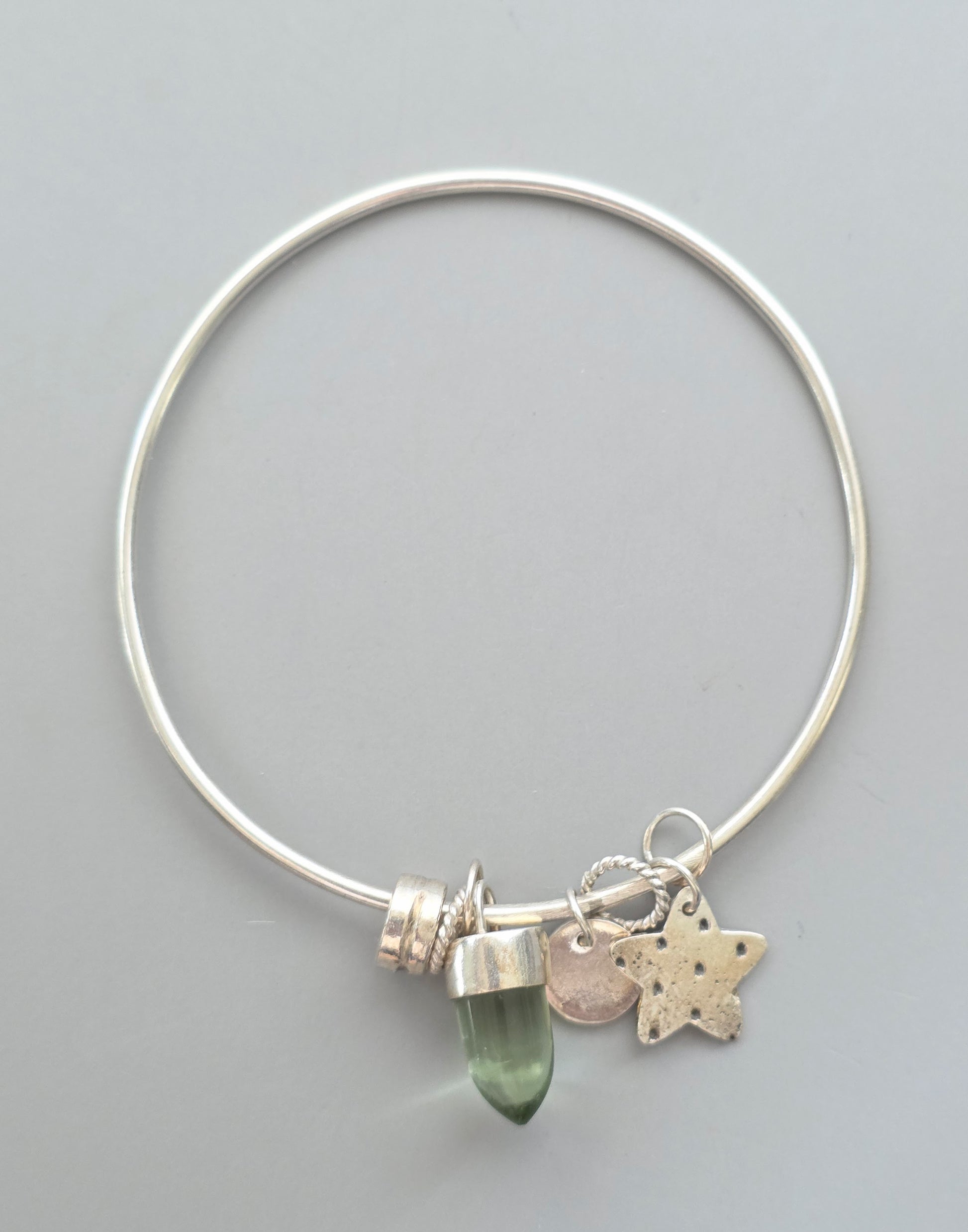 Silver bracelet with a green gemstone and star charm on a gray background